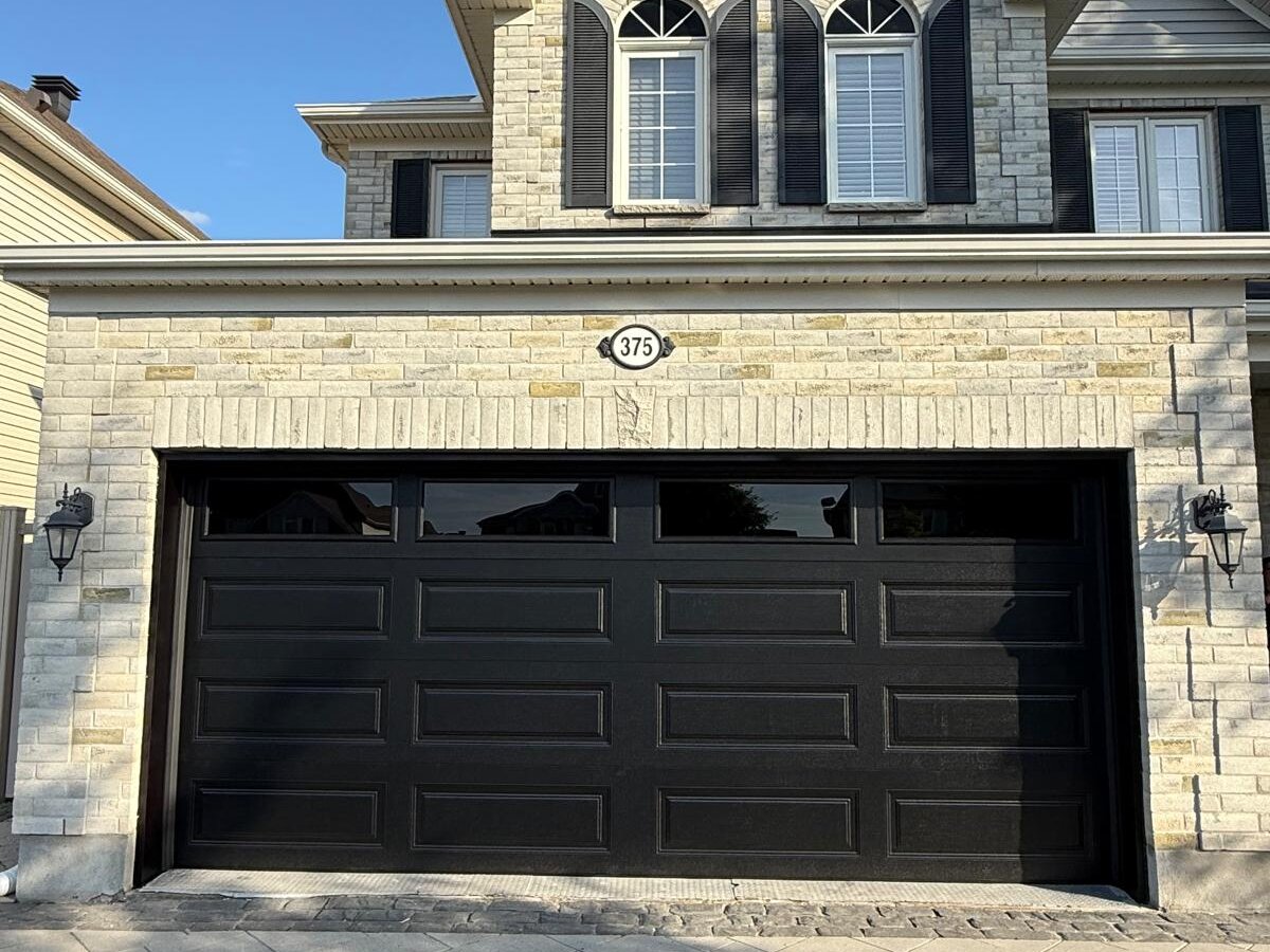 Black modern flush-panel double garage door on a stone-front Ottawa region home