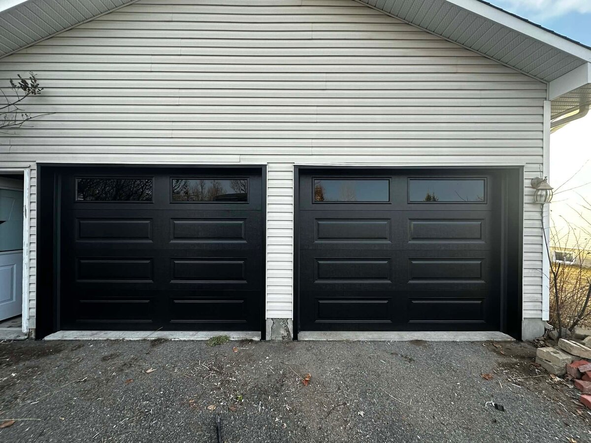 Black double garage door with window inserts on a white-sided home