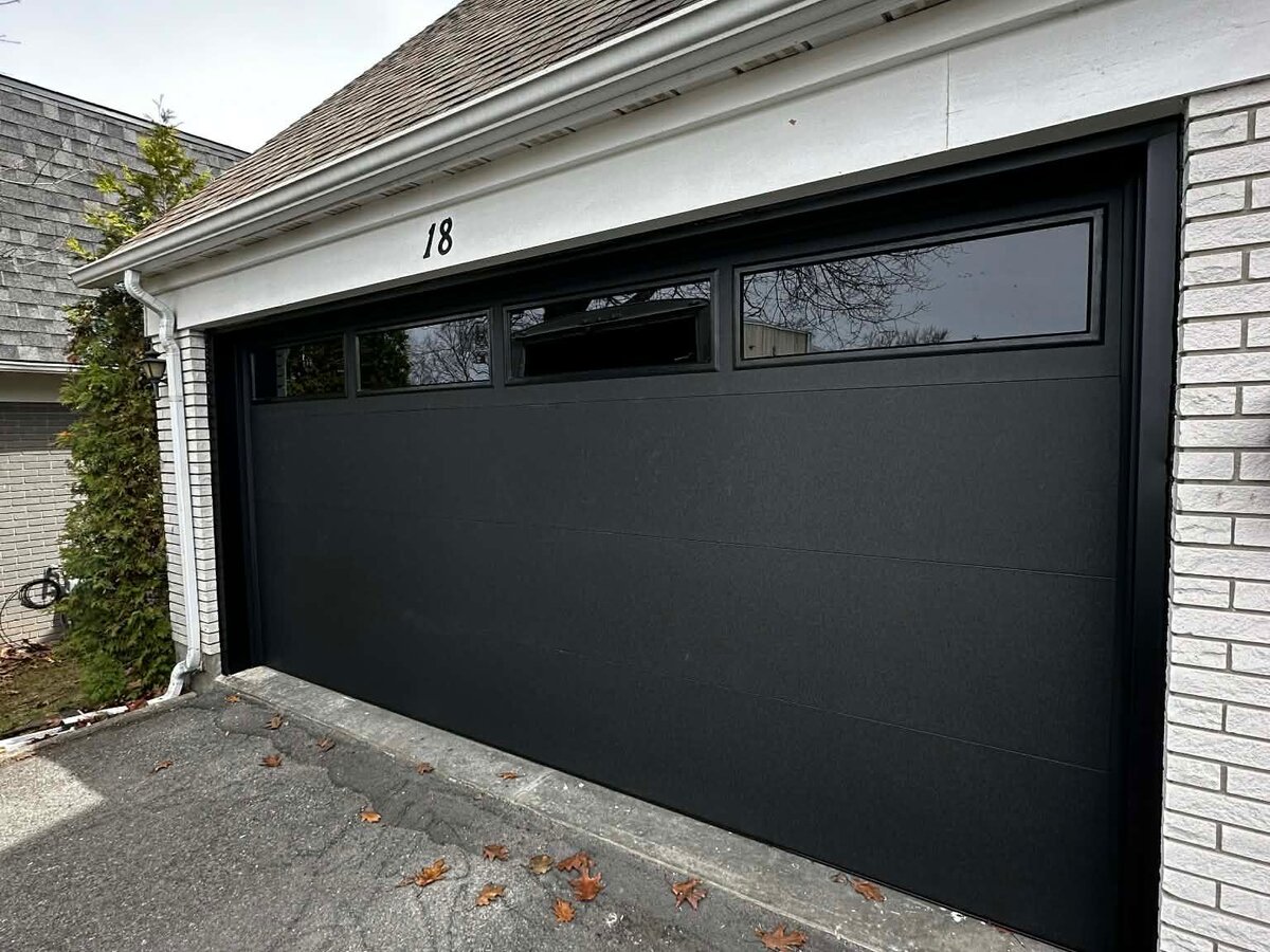 Sleek black flush-panel double garage door on a brick home