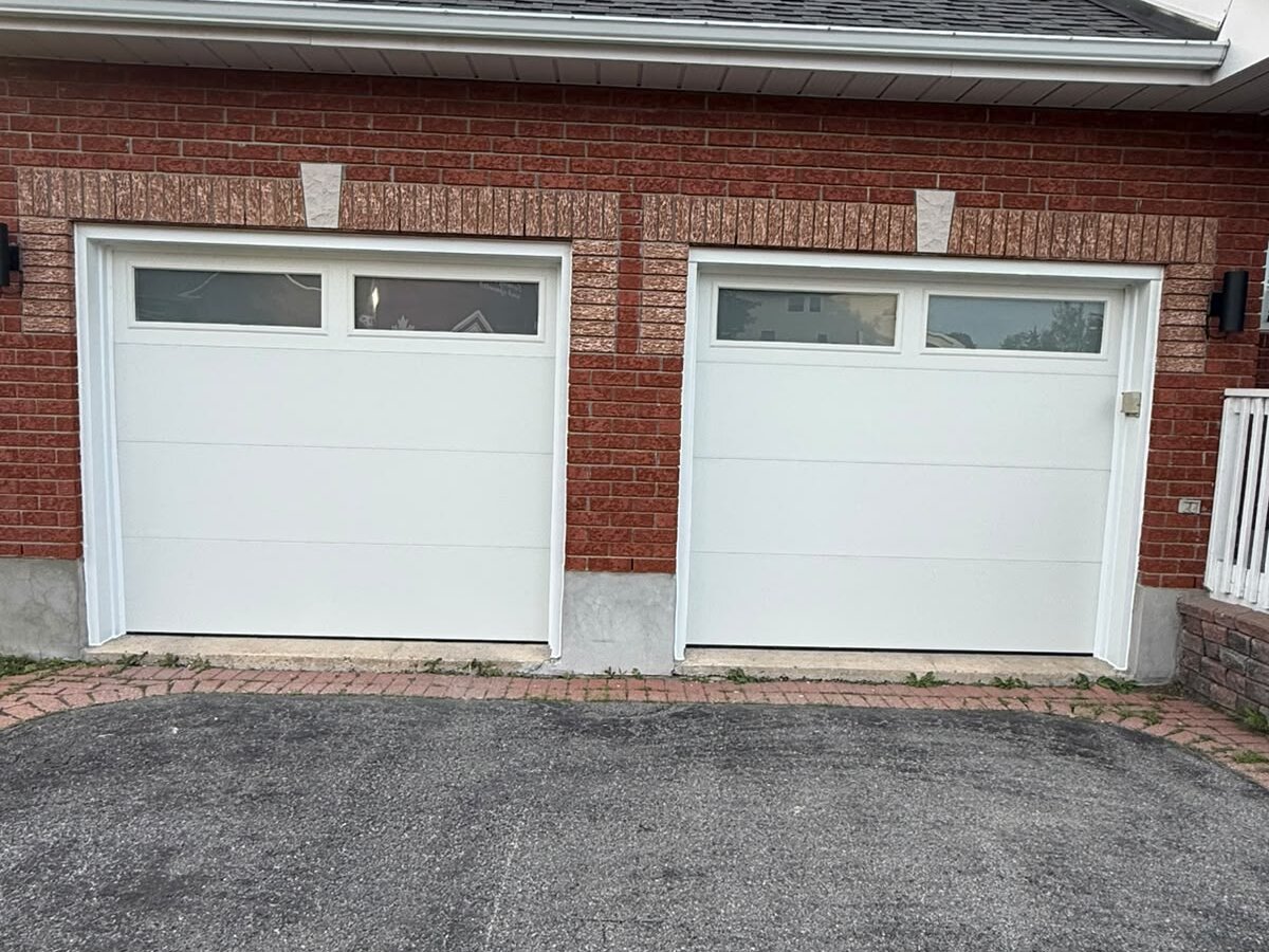 Two white garage doors with top window rows on a brick home