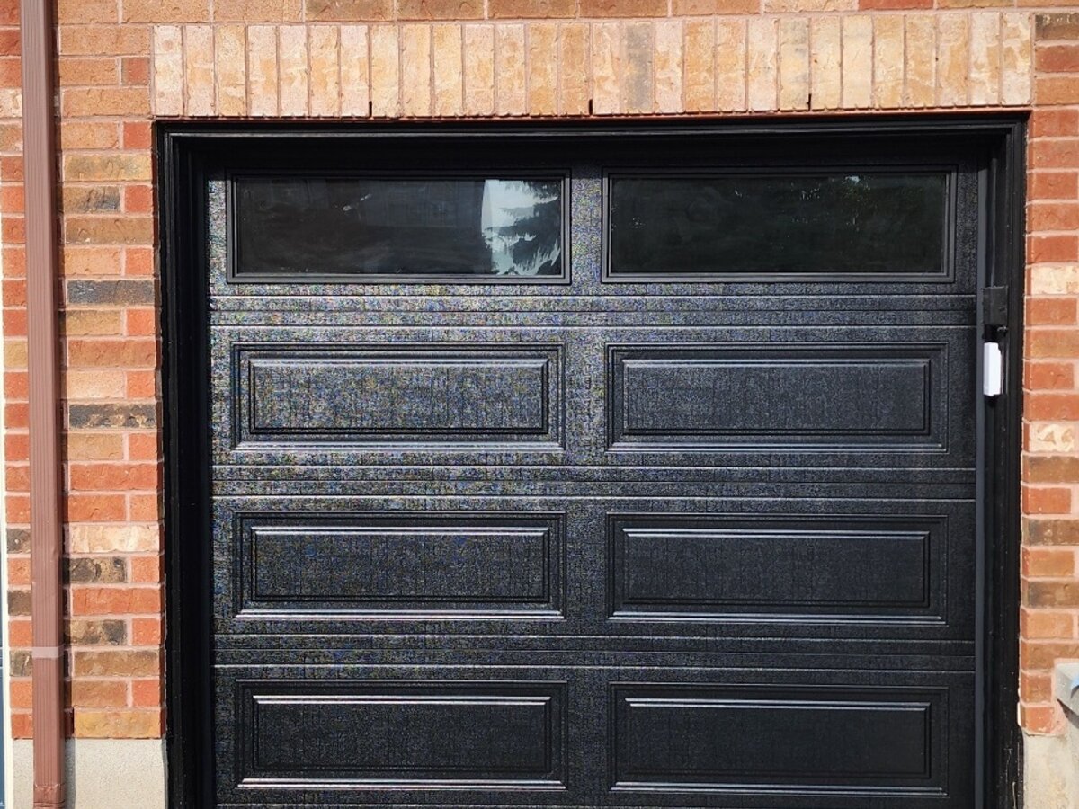 Glossy black raised-panel single garage door on a brick home