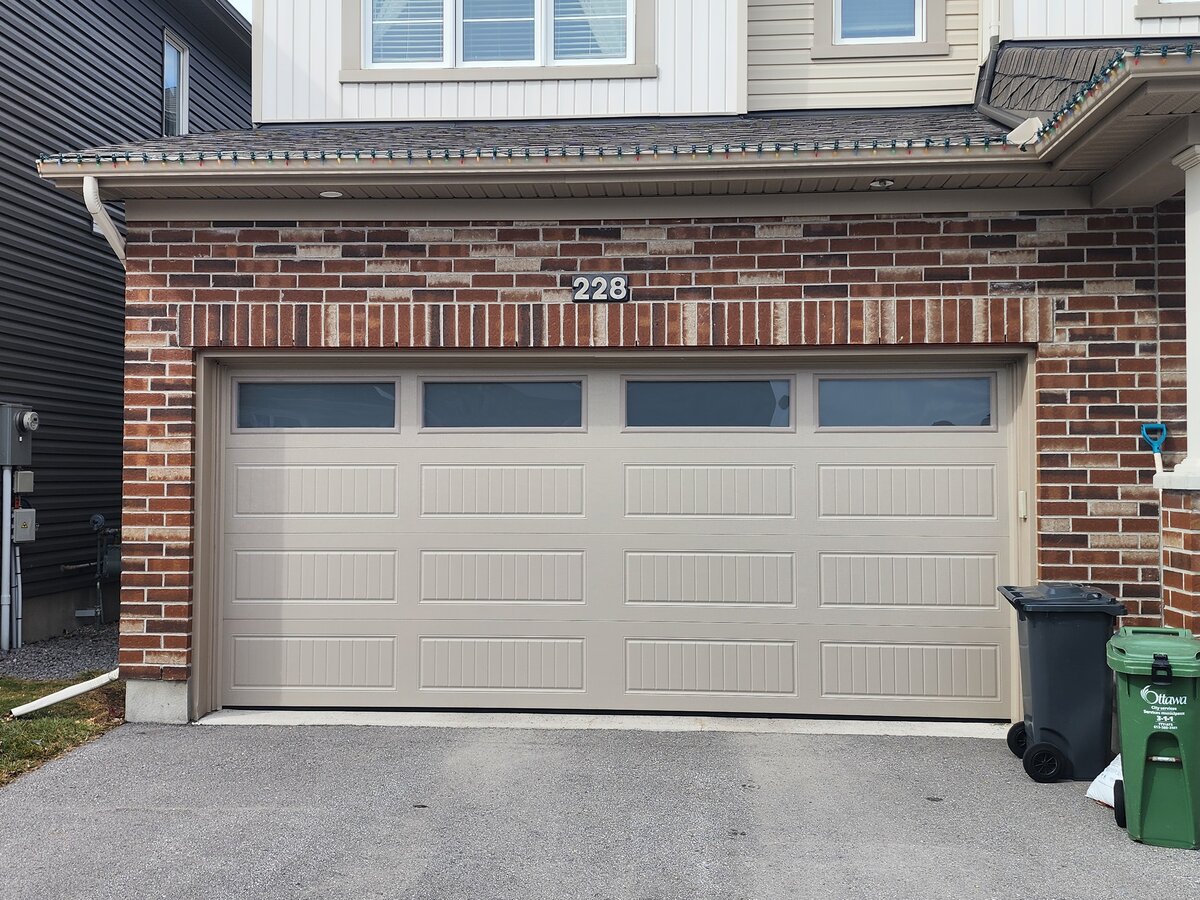 Beige almond raised-panel double garage door on a brick home