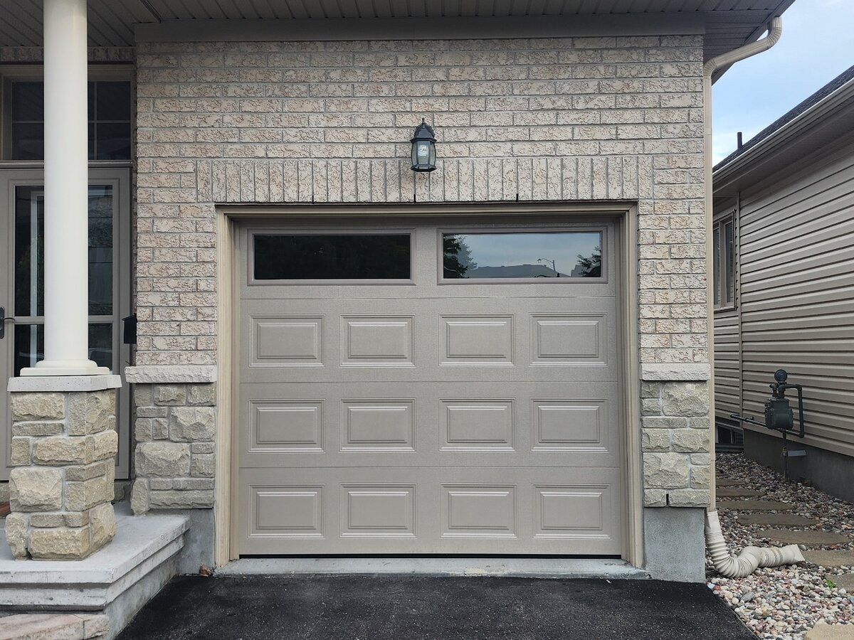 Almond raised-panel single garage door with a window row on a stone-front home