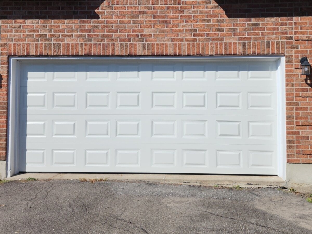 White raised-panel double garage door on a red brick home
