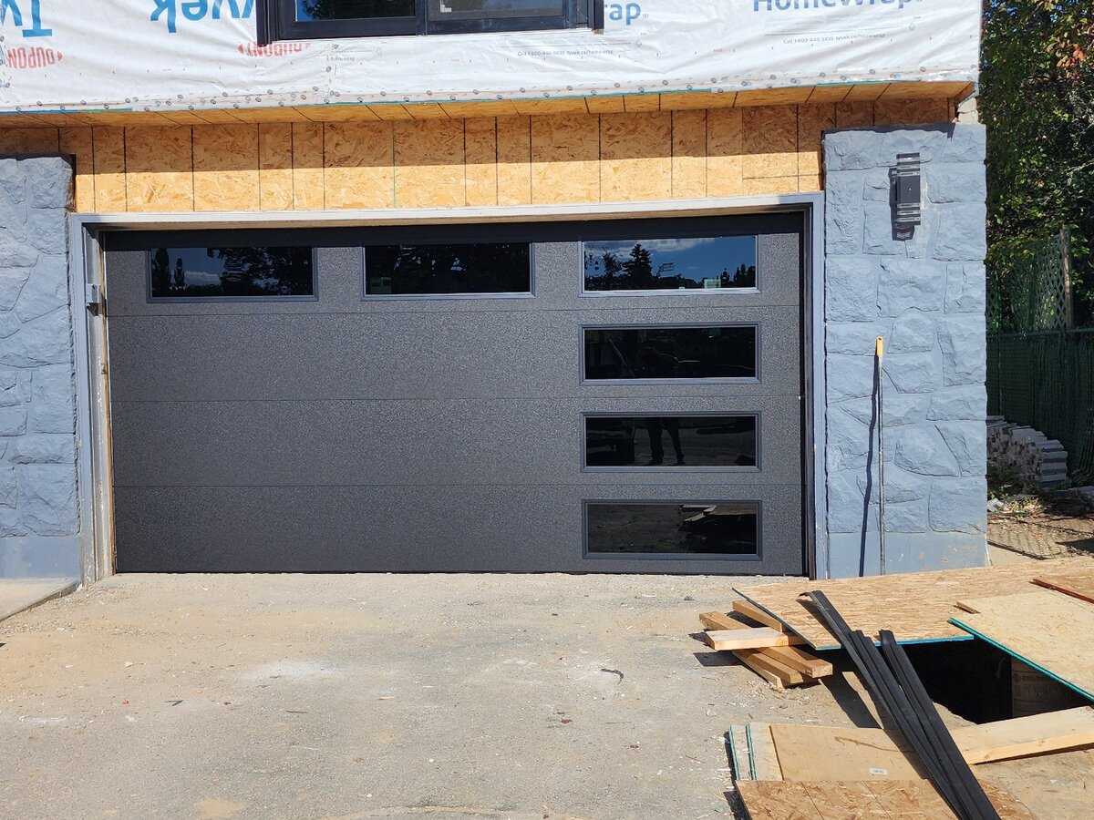 Black modern garage door with vertical glass accents on a new-construction stone home