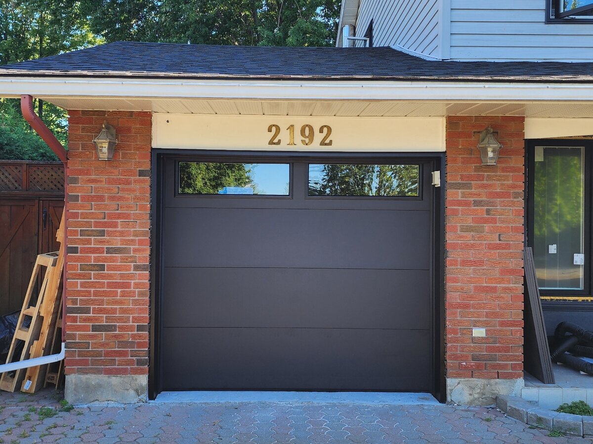 Dark brown flush-panel single garage door on a two-tone brick home