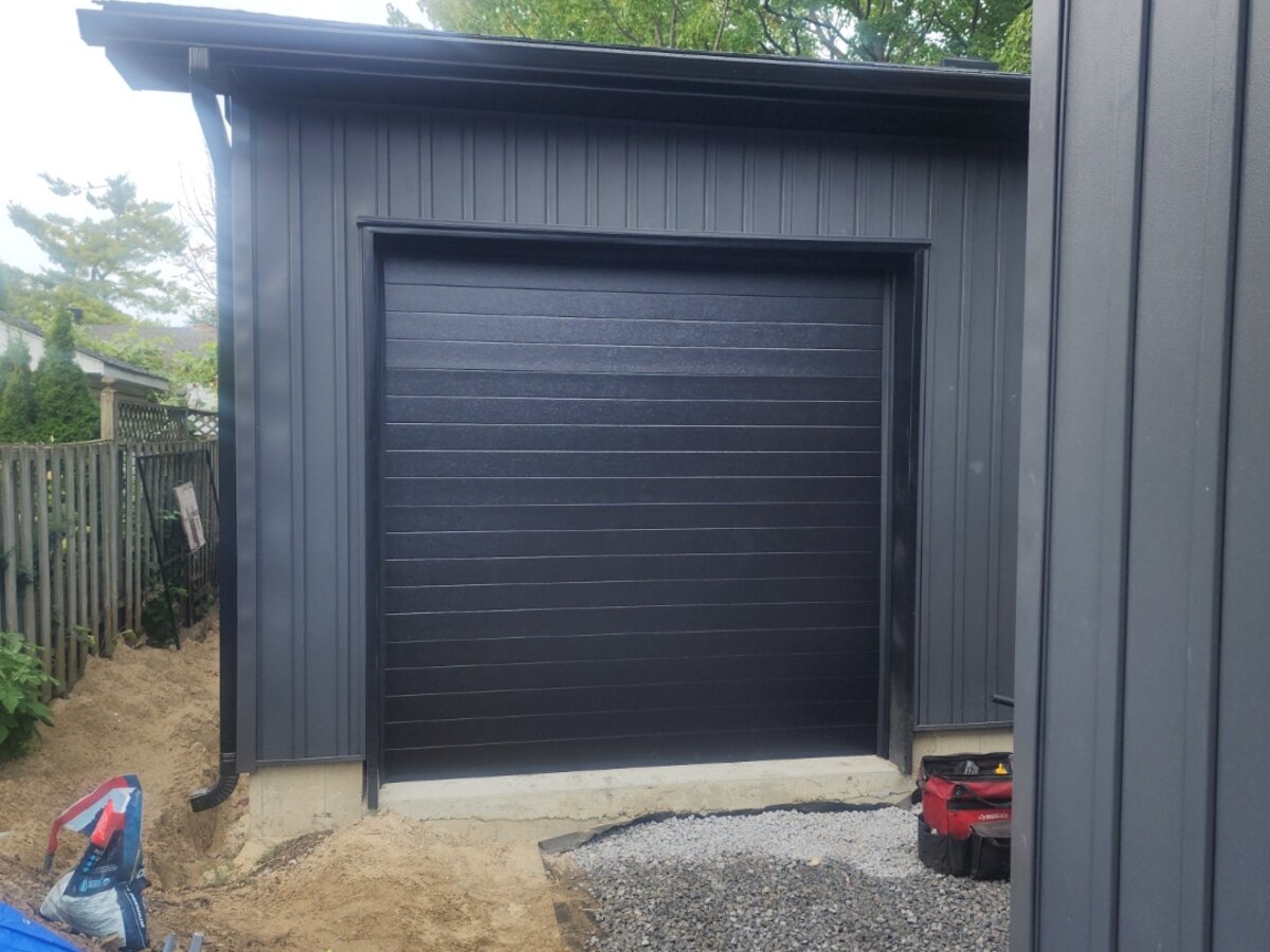 Black flush-panel single garage door on a dark-sided modern detached garage