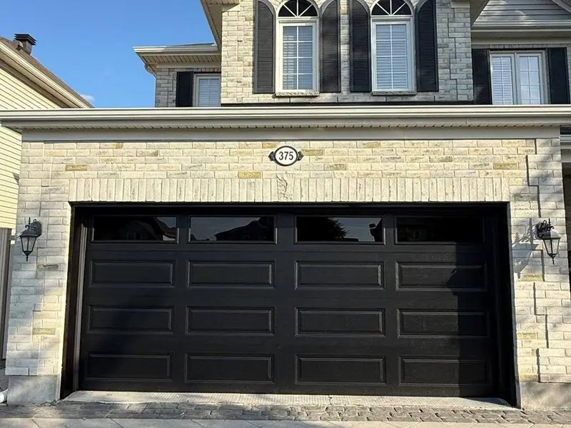 Black modern flush-panel double garage door on a stone-front Ottawa region home
