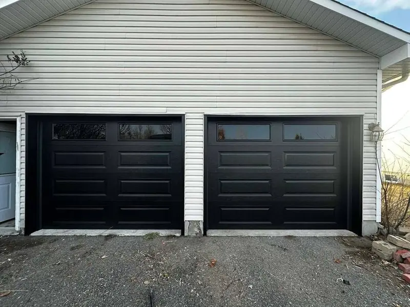Black double garage door with window inserts on a white-sided home