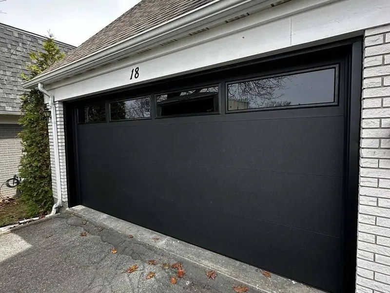 Sleek black flush-panel double garage door on a brick home