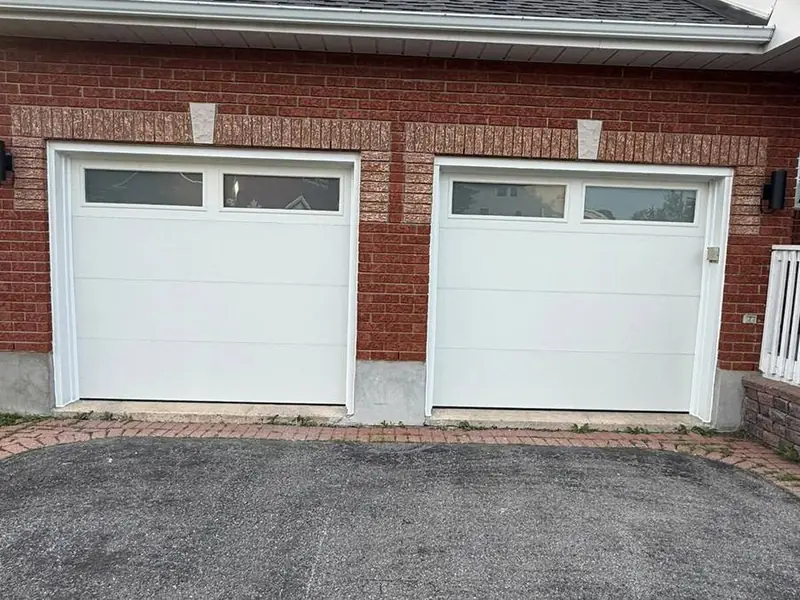 Two white garage doors with top window rows on a brick home
