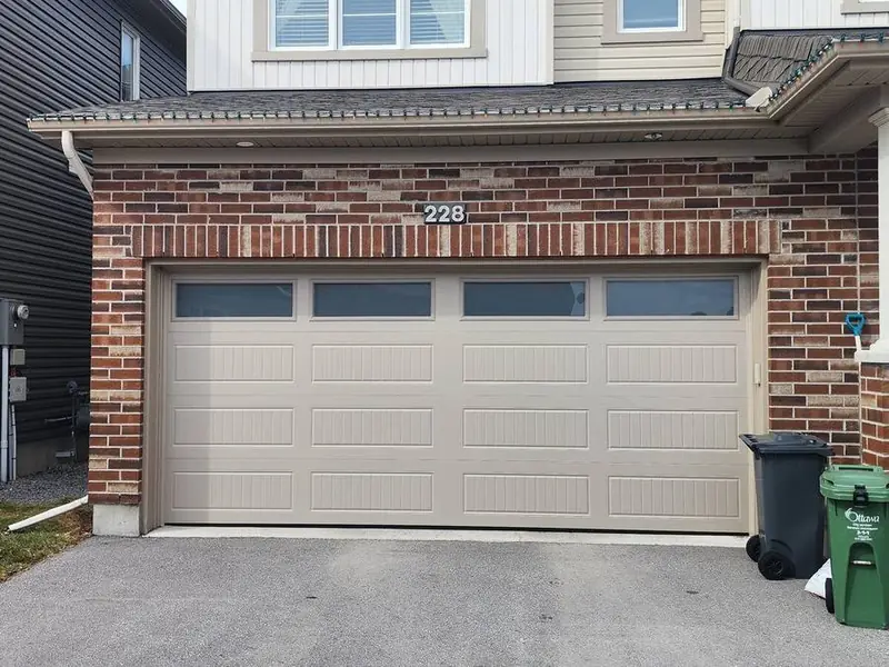 Beige almond raised-panel double garage door on a brick home