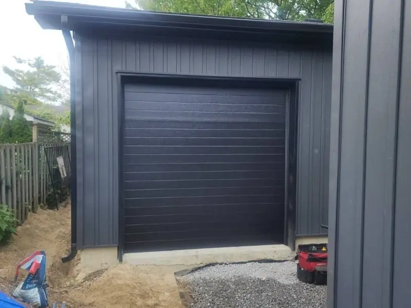 Black flush-panel single garage door on a dark-sided modern detached garage