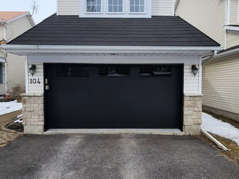 Black raised-panel single garage door on a home with a dark roof