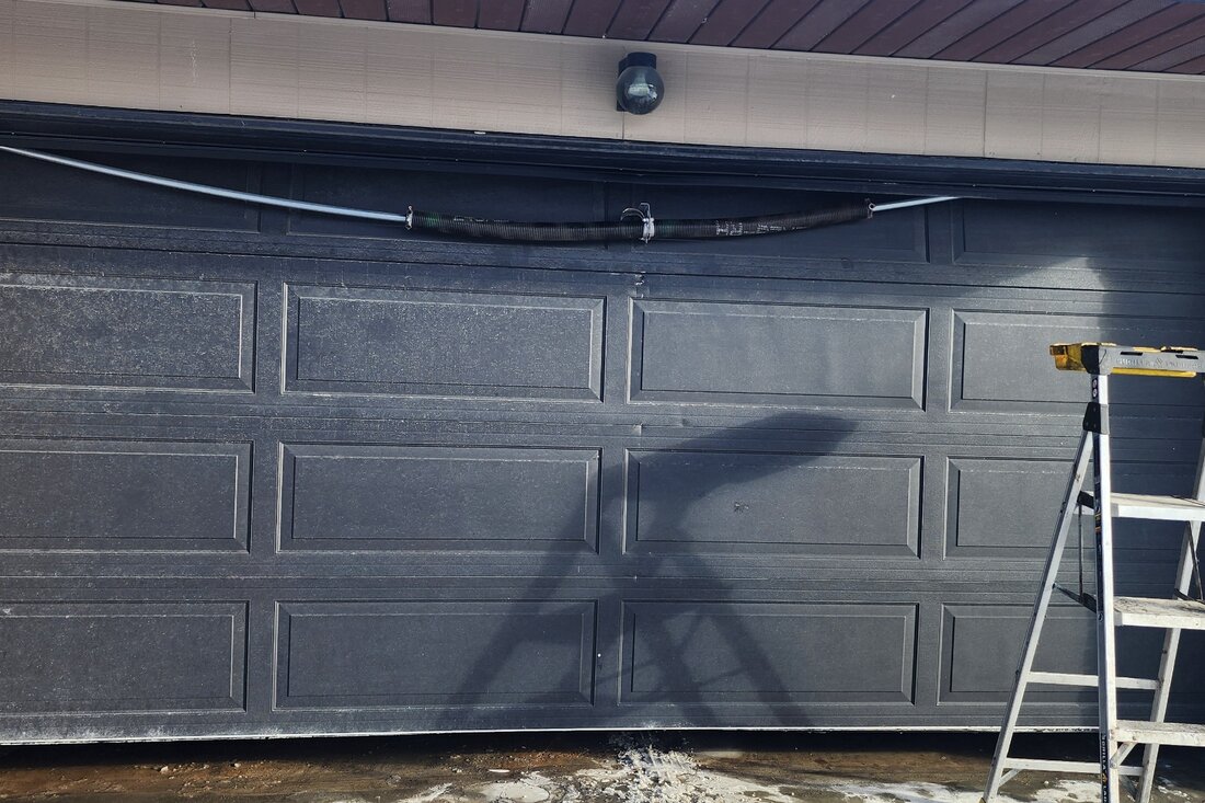 DPS Garage Doors repairing the torsion spring on a dark double garage door with a ladder set up in Ottawa